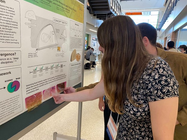 Image description: Two people feel the biopolymers that are attached to the PEELS poster.